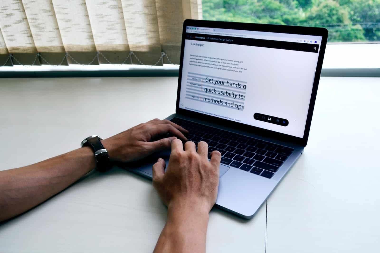 person using macbook pro on white table